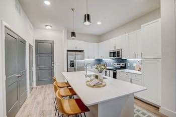 A modern kitchen with a long white island and wooden chairs.